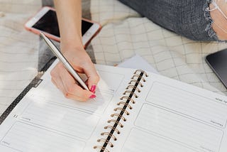 Cropped woman sitting on blanket taking notes in a weekly planner. Create an ideal week template.