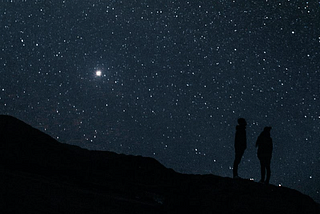 A couple standing in silhouette against the stars