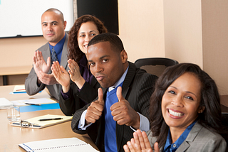 four people clapping and smiling with one giving the thumbs up