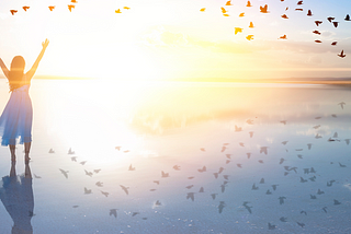 Woman with raised hands near the ocean, birds flying above, representing freedom and growth