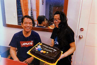 My father and I on my 28th birthday in 2022. We’re both smiling. I’m holding a chocolate cake with “Happy Birthday, Jonnah” written on it.