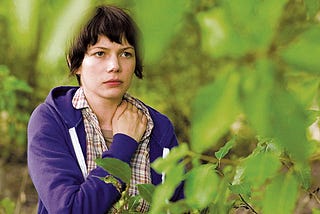 A woman in a blue jacket stands amidst trees.