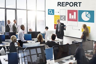 Senior business leader in front of white board with data talking to a room full of diverse employees.