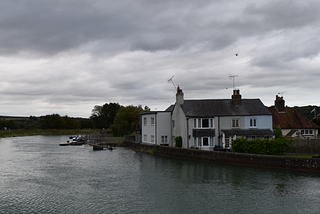 Stone house bordering a wide river under a gray, clouded sky — Moral Letters to Lucilius