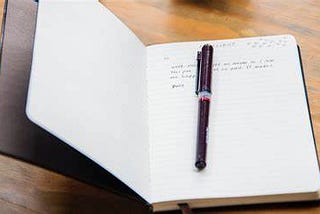 An open journal with some writing and a pen.