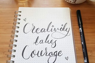 A coiled notebook with words ‘Creativity takes courage’ written in cursive