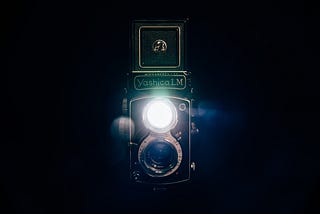 Late 50s Japanese dual lens camera against a dark background with the top lens emitting a bright light.