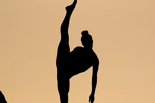 Silhouette of a person in front of amber background doing standing splits with ground leg (left leg) hyperextended.
