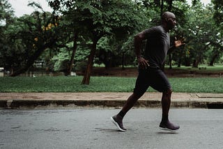A man jogs along a quiet park road, surrounded by lush greenery, embodying dedication to fitness, outdoor exercise, and a healthy lifestyle. Reflecting the perspective of Ramneek Bhogal on why men over 40 should rethink their wellness routine.