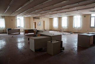 An abandoned, somewhat eery office interior with empty desks, no chairs and dim lighting.