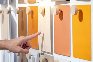 Designer hand pointing at colorful laminate sheet on material swatch wall display in material library.