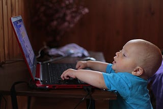 Toddler reaches to type on an open laptop