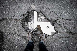 Image of a puddle reflecting skyscrapers and an airplane