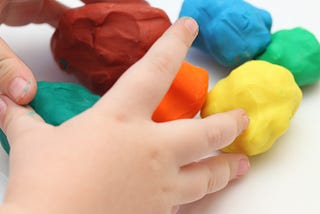 child’s hands playing with playdough of different colors.
