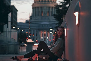 Woman posing, sitting on the ground in Madison, Wisconsin with the capital building in the background.