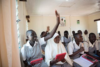 Grade 8 girls in Kenya raise their hand in class discussion while holding their tablets to learn.