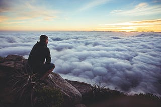 Man on a mountain top overlooking a beautifl sunrise.