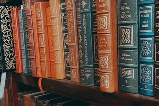 Antique hardcover books in various colors sit in a bookshelf