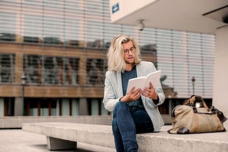 Long white haired formally dressed man reading a book outdoors