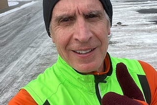 An older man in bright running clothes and black beanie gives a thumbs up