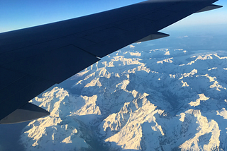 The wing of a plane flying over snowy mountains.