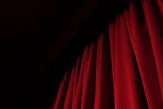 A red theater curtain disappearing up into the dark.