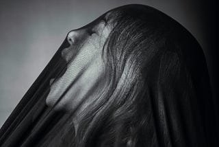 A black white photo shows a woman screaming under a see through veil.