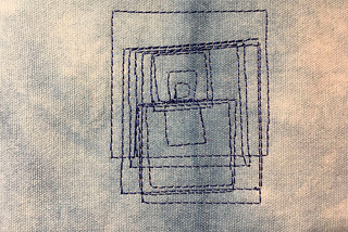 A group of overlapping squares embroidered in dark blue thread on a light blue cloth