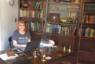 Woman at desk in office library with bookshelves and rolling ladder.