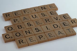 Scrabble tiles spelling the words “REFINE”, “PAUSE”, “OBSERVE”, “CONSIDER”, and “REPEAT”.