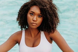 Photo of African American woman with white tank top looking in a questioning way toward viewer.