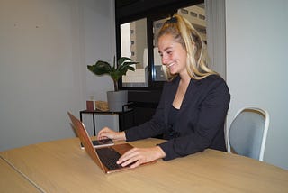 Sharissa behind her laptop in her old office. This image is decorative for the blog “Why do people always think I’m a freelancer?”