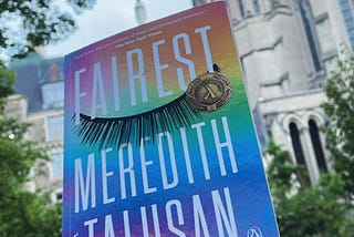 The cover of Fairest by Meredith Talusan, a memoir, is a rainbow gradient starting with pink and orange and yellow, then green, blue and purple, with a set of closed eyelashes after the title, Fairest.