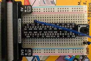 Breadboard connected to Raspberry Pi breakout board with circuit showing pushbutton, resistor and jumper wire.