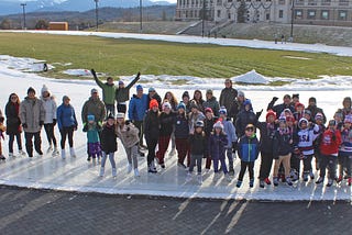 Photo of several World Ice Skating Day participants standing on the outdoor Olympic Speed Skating Oval and smiling.