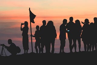 A group of people contemplating the Tanah Lot Temple in Indonesia with a sunset background