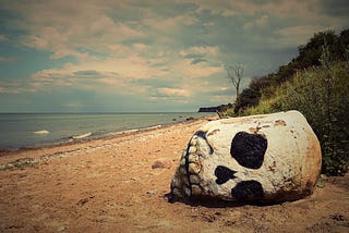 Rock painted in image of skull, sideways on beach.