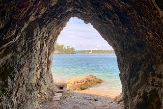 A view through the opening of a cave onto a beach and blue-green sea.