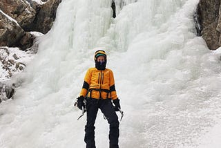 an ice climber standing in front of a frozen water fall holding their ice tools