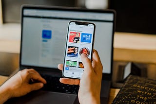 Person holding a phone with several icons of podcasts avaialble for listening.