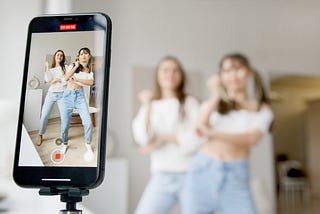 Women in White Shirts and Blue Denim Posing in Front of Smartphone.