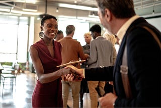 A woman in a red dress holding a clipboard and shaking a mans hand