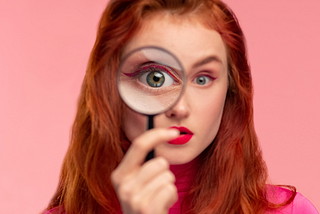 Red headed woman looks through a magnifying glass.