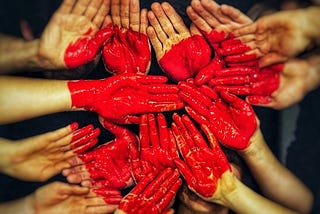 many hands held together with a bright red heart painted across all the hands making up different parts of the heart