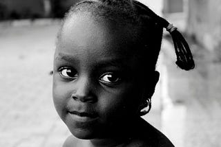 A black-and-white photo of a beautiful black girl looking into your eyes. This depicts how I’d sit my younger self down and share this story if I was told earlier.