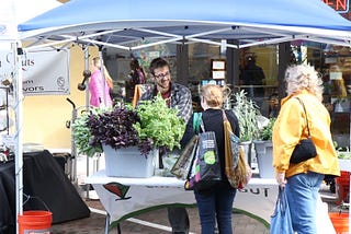 A farmer at his farmers market stall talking to two customers