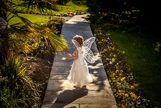 A little girl in a garden, dressed up as a fairy.