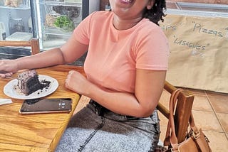 woman wearing a pink crop to and denim skirt, enjoying vegan chocolate cake.