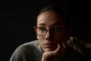 Woman with glasses, with her head propped on her hand, seemingly lost in thought.