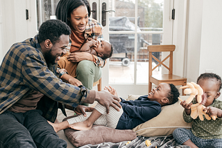 Parents shown with young children. Mother feeding a baby, father helping another child, and a third playing with a toy.